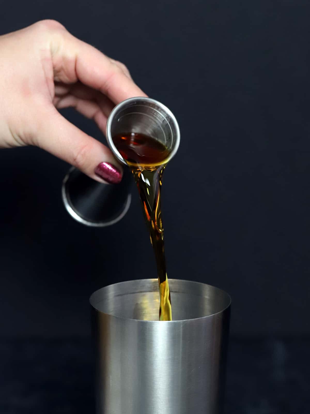 Dark rum being poured into a cocktail shaker.