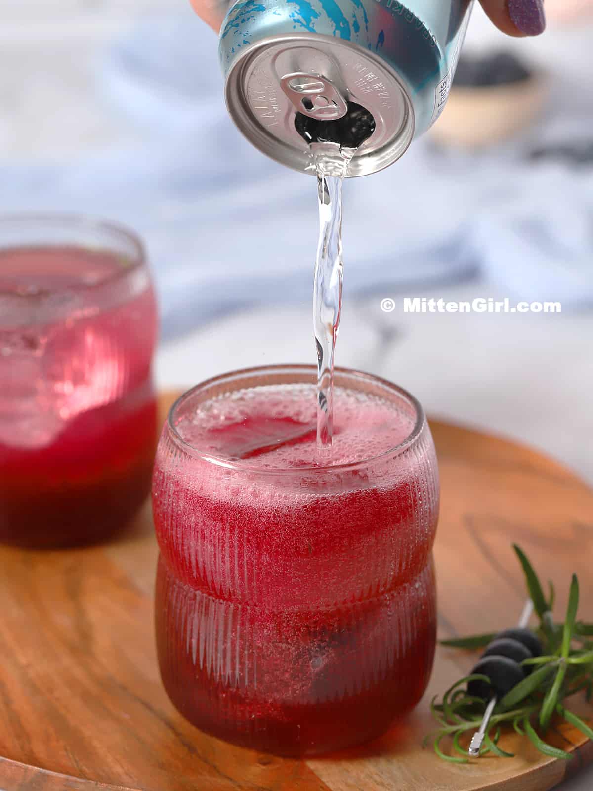 Club soda being poured into a glass filled with blueberry grapefruit mocktail. 