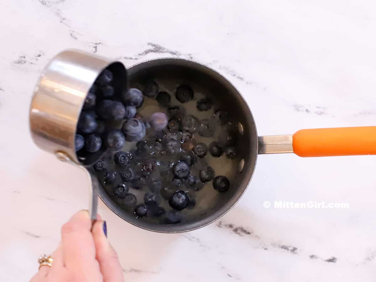 Blueberries being poured into a pot of water and sugar. 