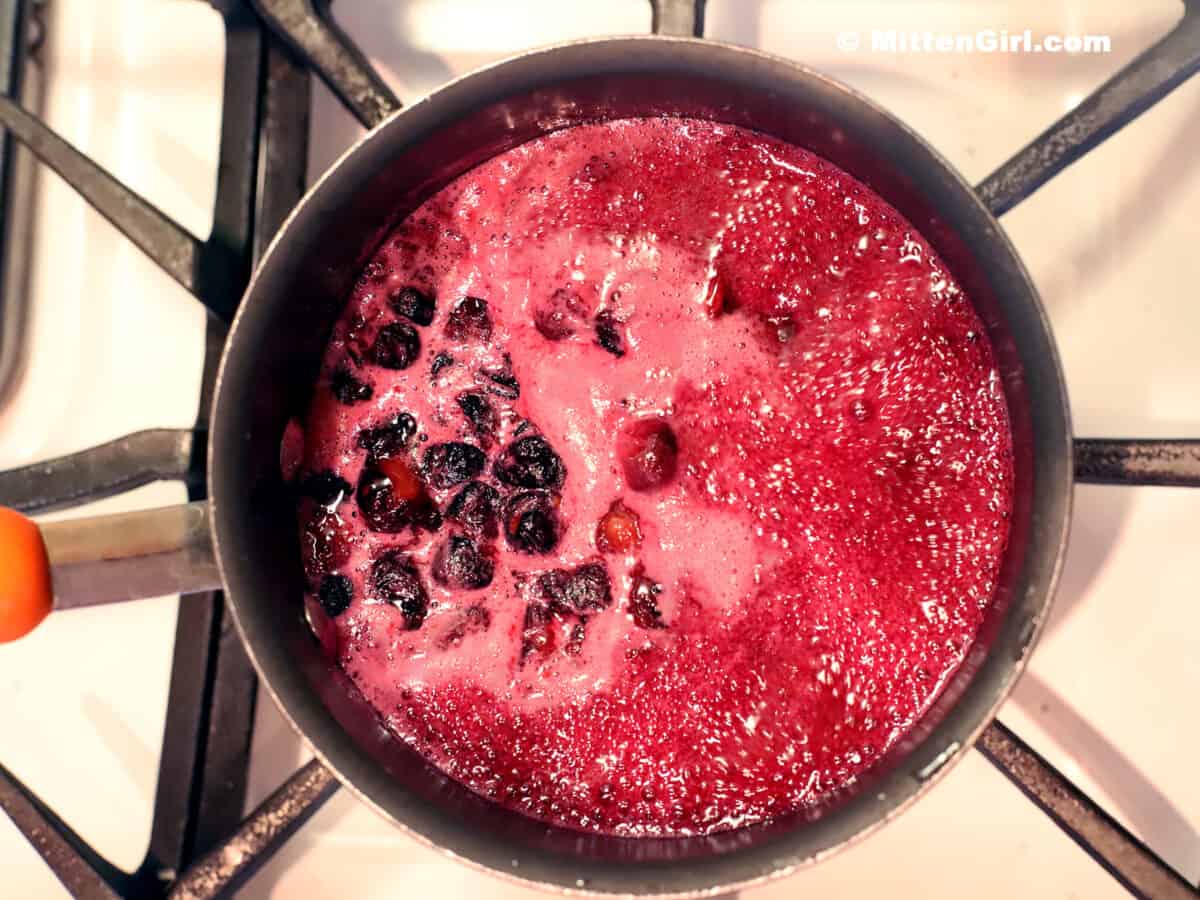 Hot blueberry syrup foaming up in a pot on a stove. 