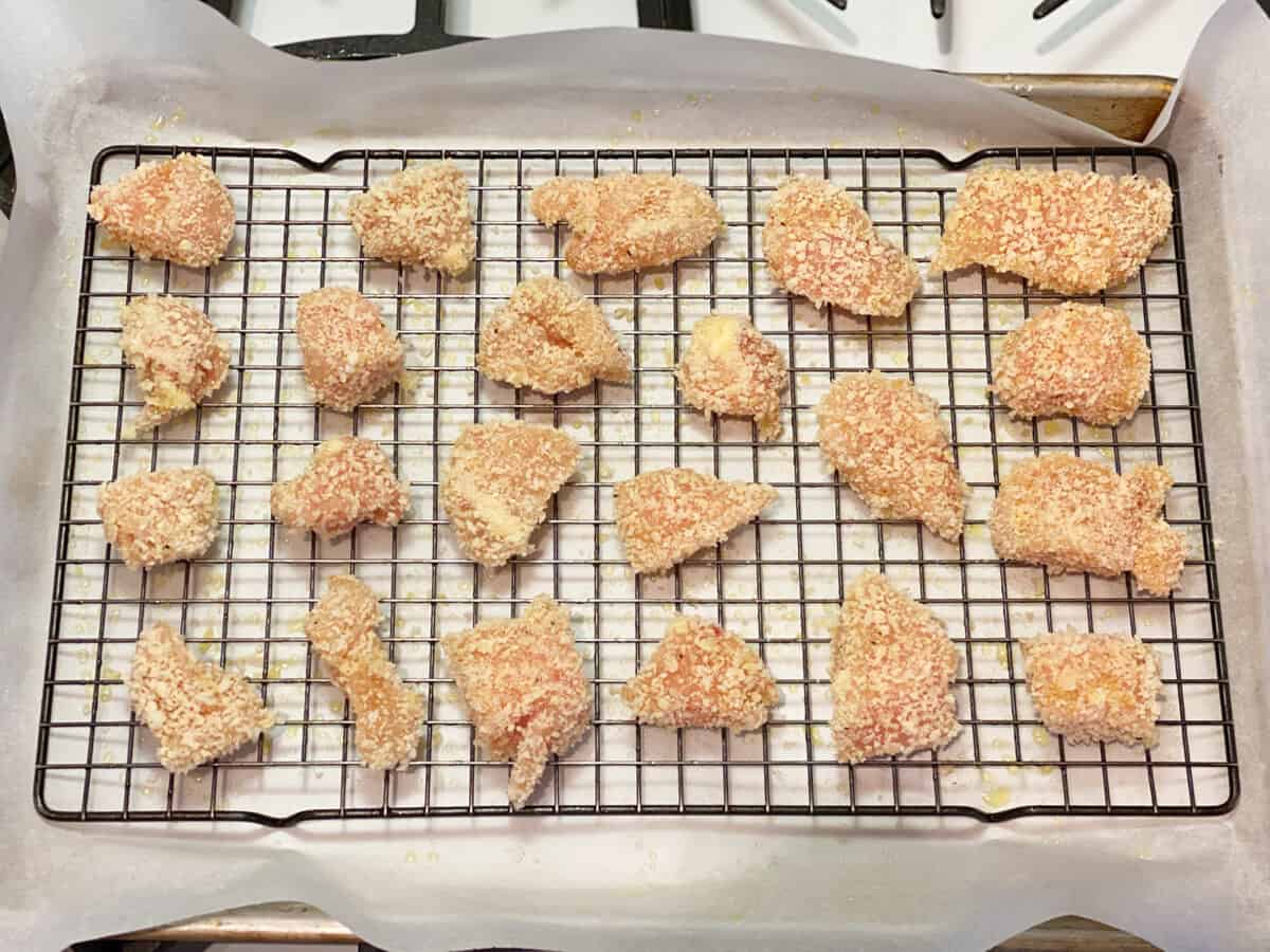 Raw, breaded, chicken cubes on a baking sheet. 