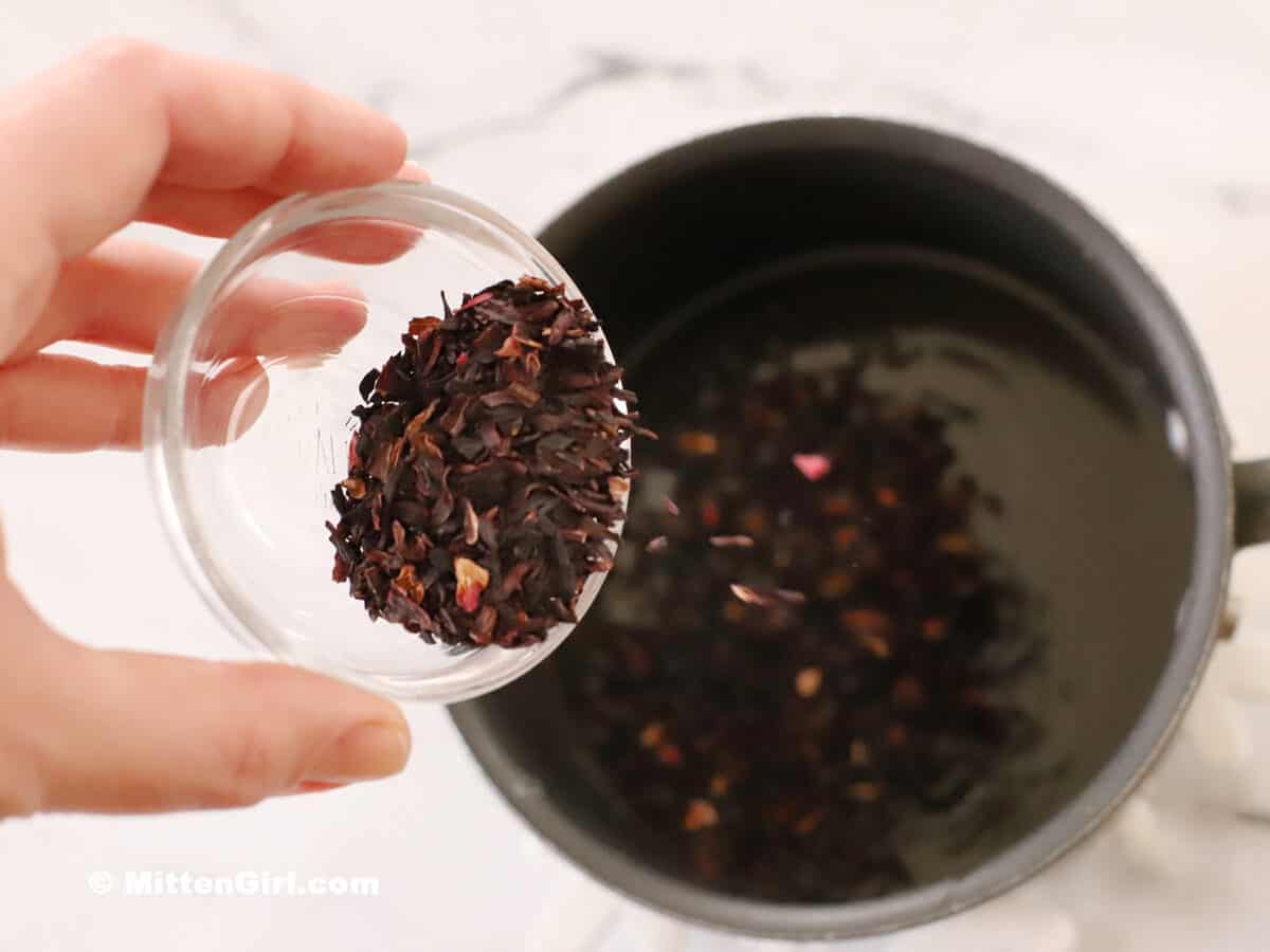 Pouring dried hibiscus flowers into a small pot of syrup.