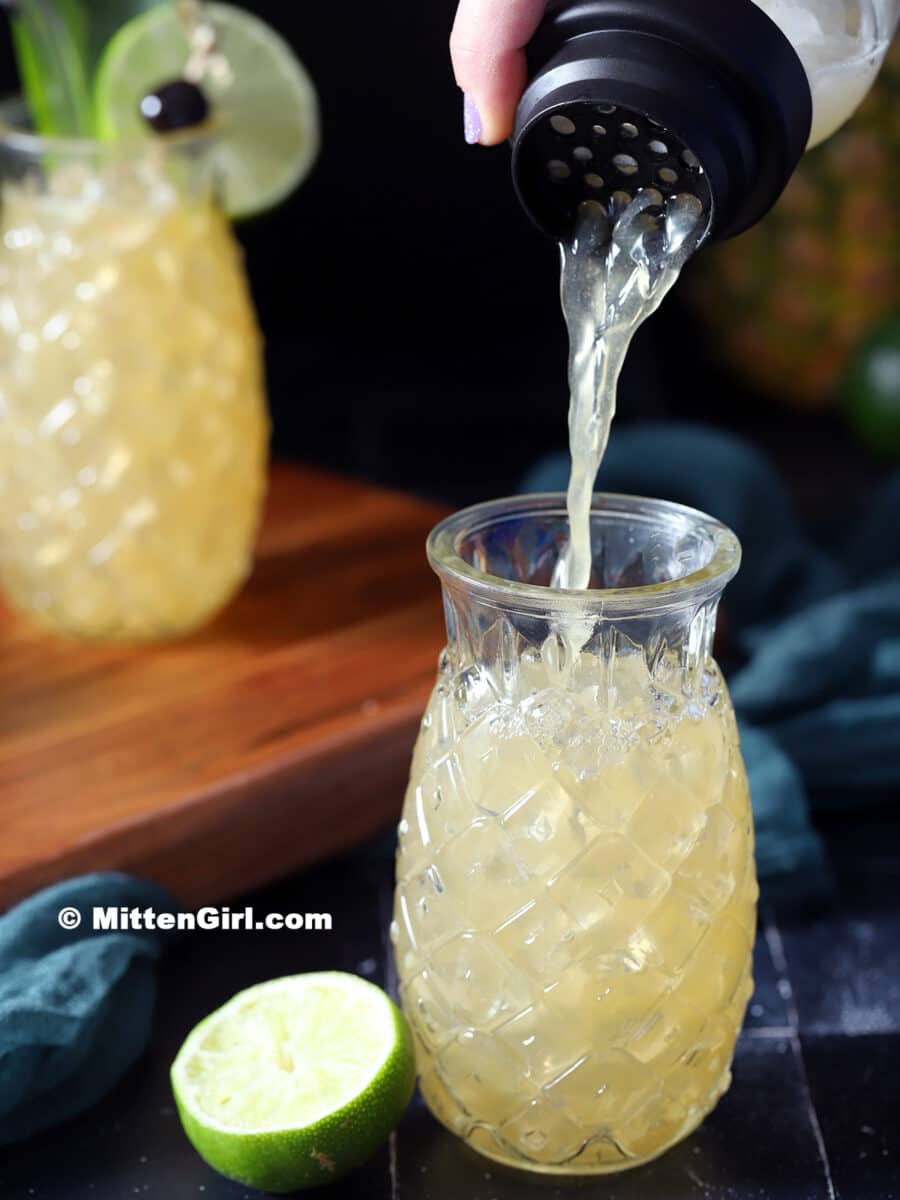 Pouring a Mai Tai into a pineapple glass filled with ice.