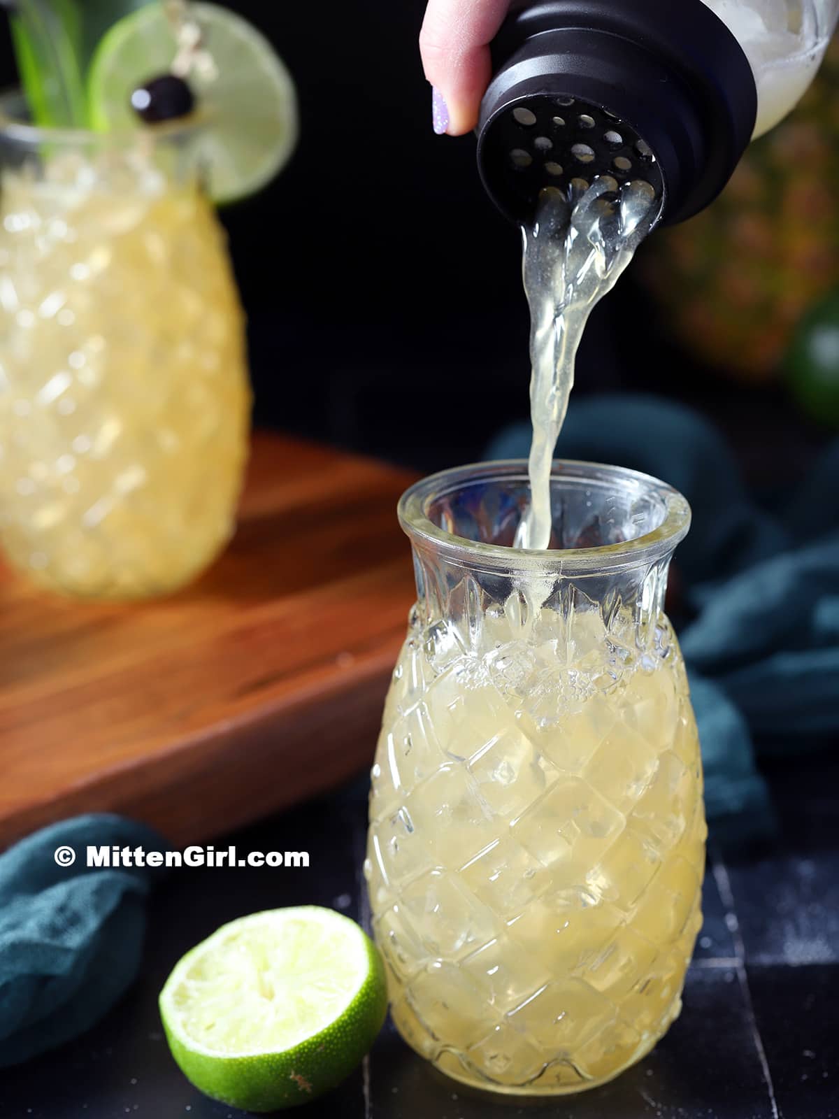 Pouring a Mai Tai into a pineapple glass filled with ice. 