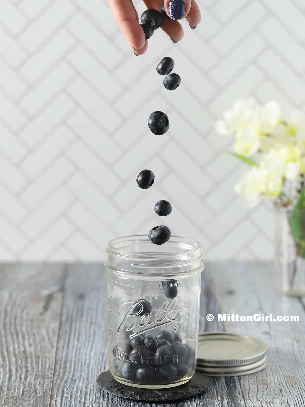 Blueberries falling into a pint jar.