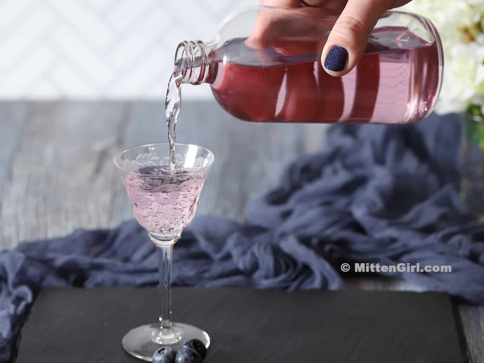 A bottle of blueberry vodka being poured into a small glass.