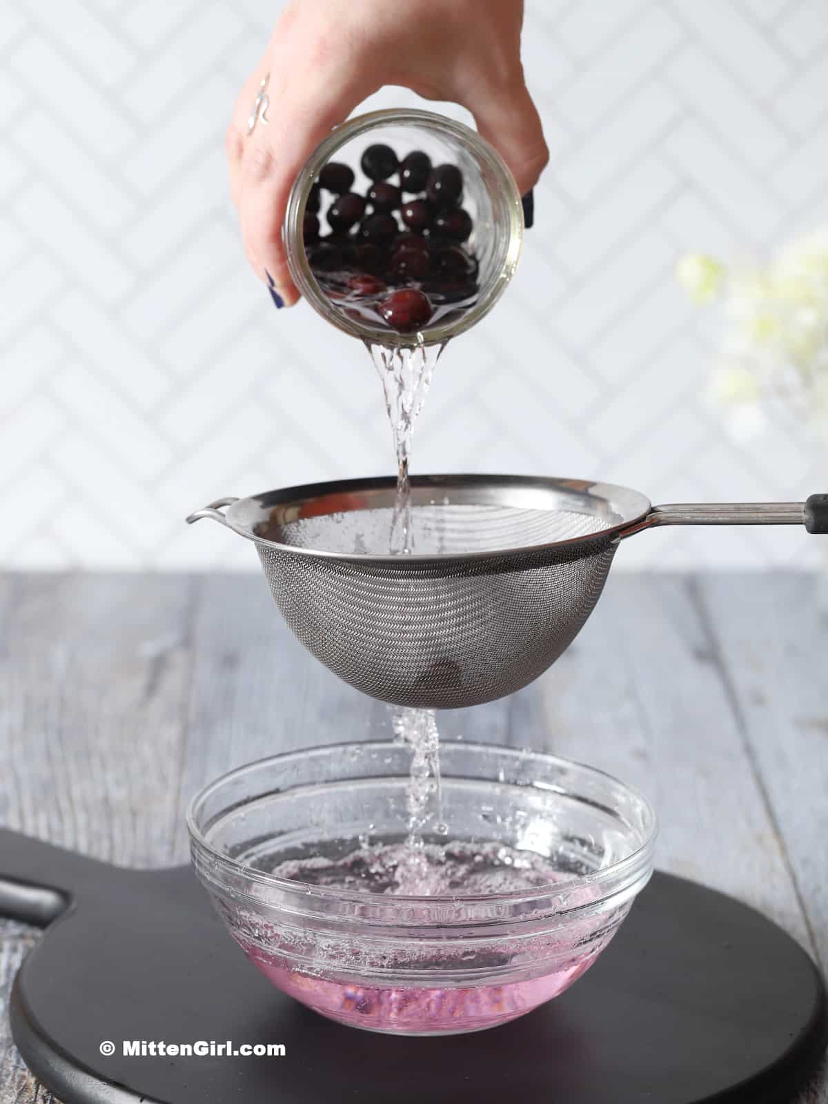 Blueberries and vodka being poured through a strainer into a bowl below.