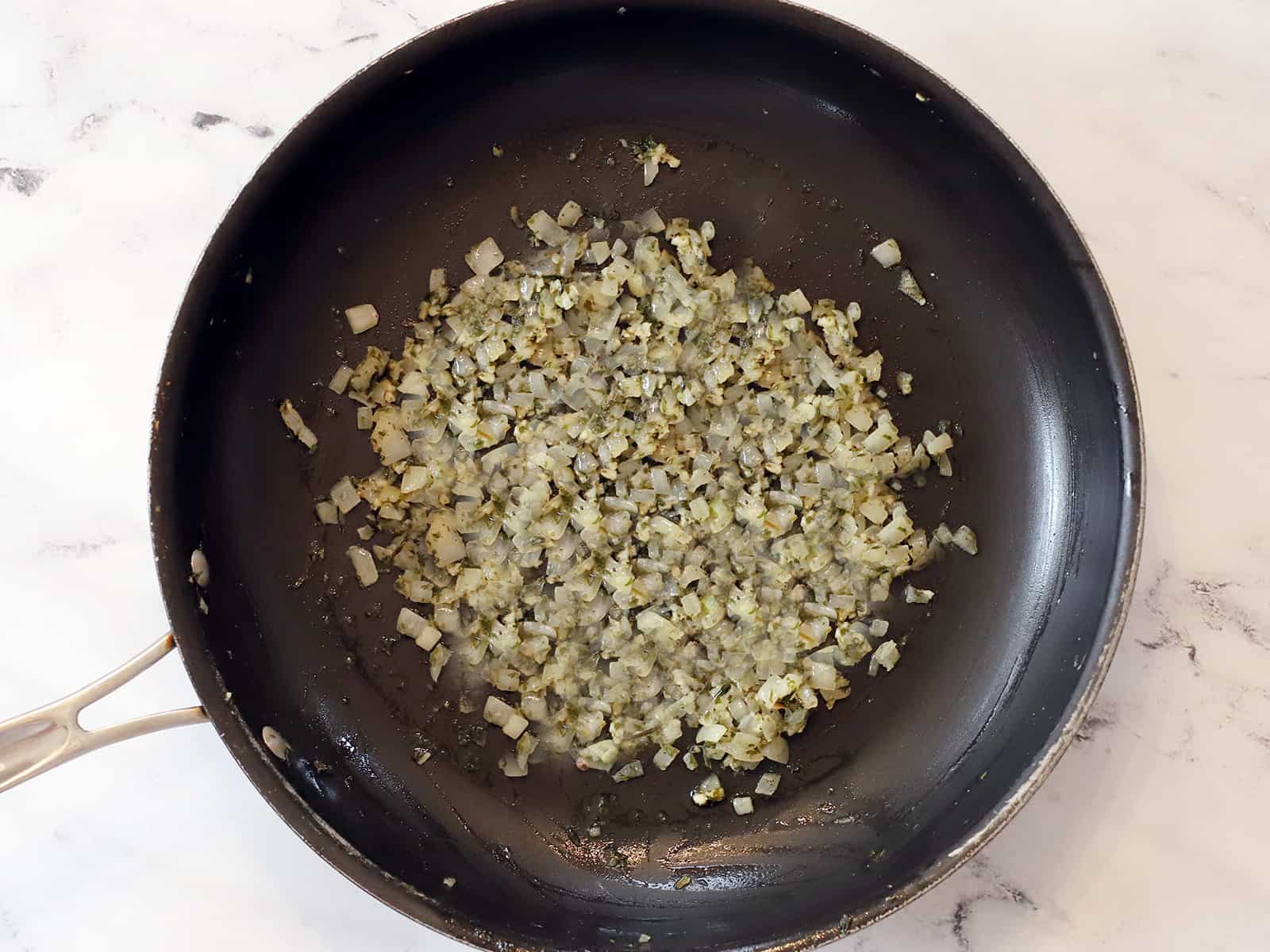 A skillet full of cooked onion, garlic and parsley. 