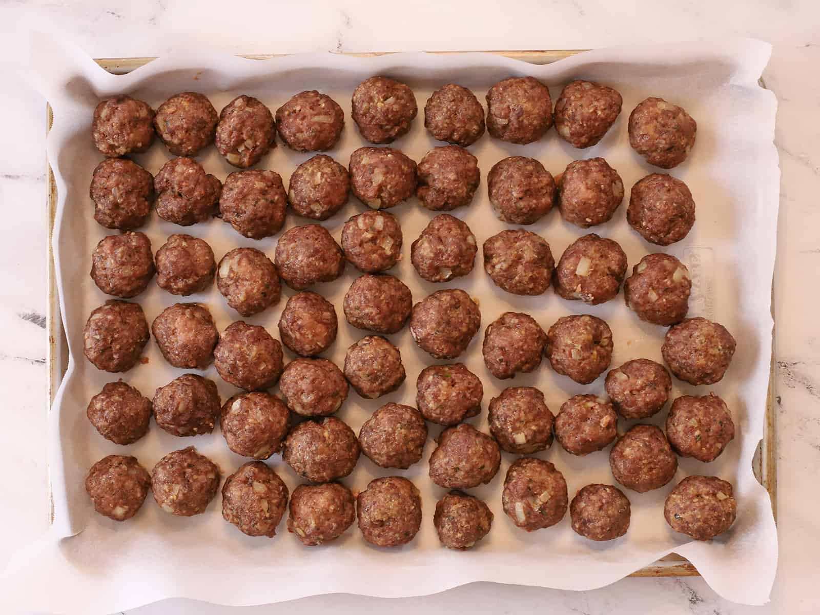 Meatballs on parchment paper on a tray, ready for the freezer.