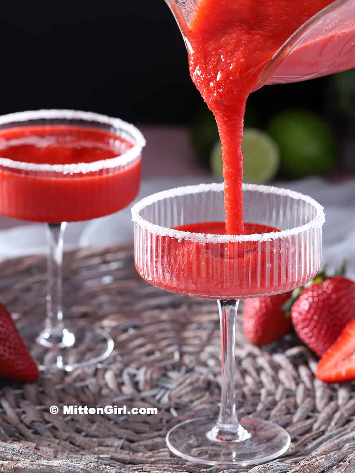 Pouring frozen strawberry daiquiri mocktail into a sugar-rimmed glass.