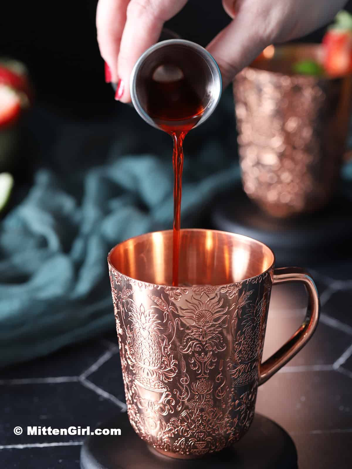 Strawberry syrup being poured into a copper mug. 