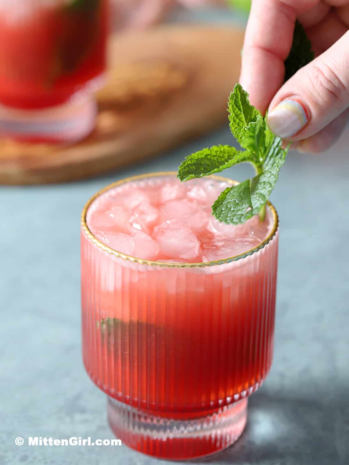 Garnishing a watermelon strawberry mocktail with a sprig of mint. 