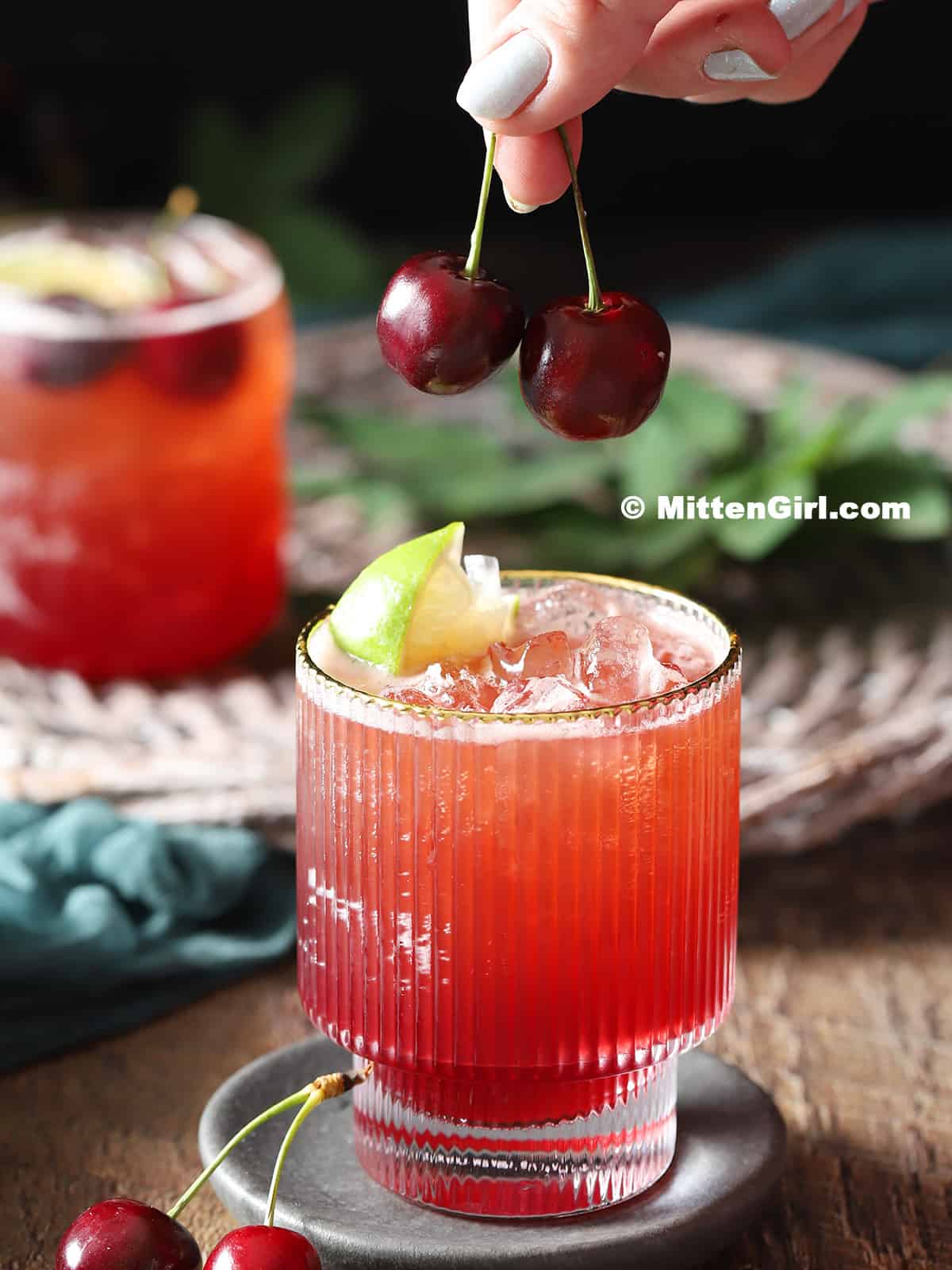 Two cherries being placed on top of a glass filled with mocktail. 