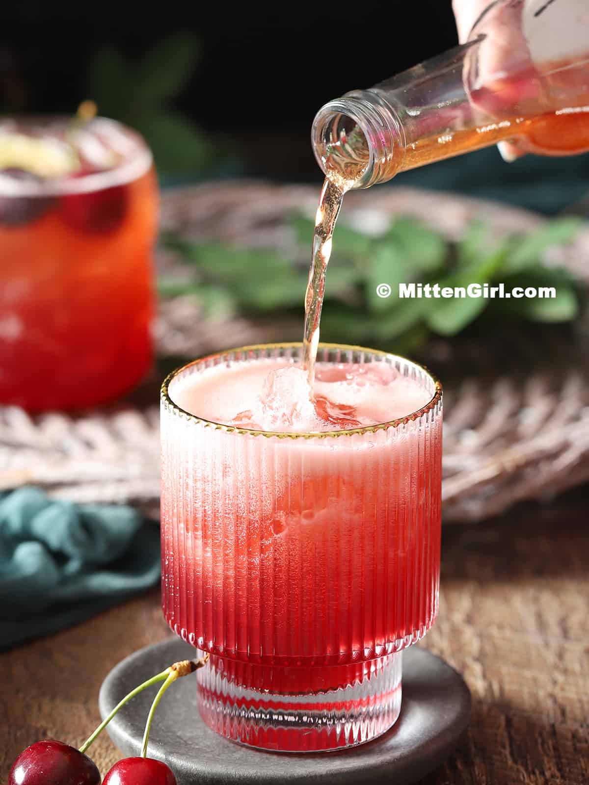 Cherry tonic water being poured into a glass filled with mocktail. 