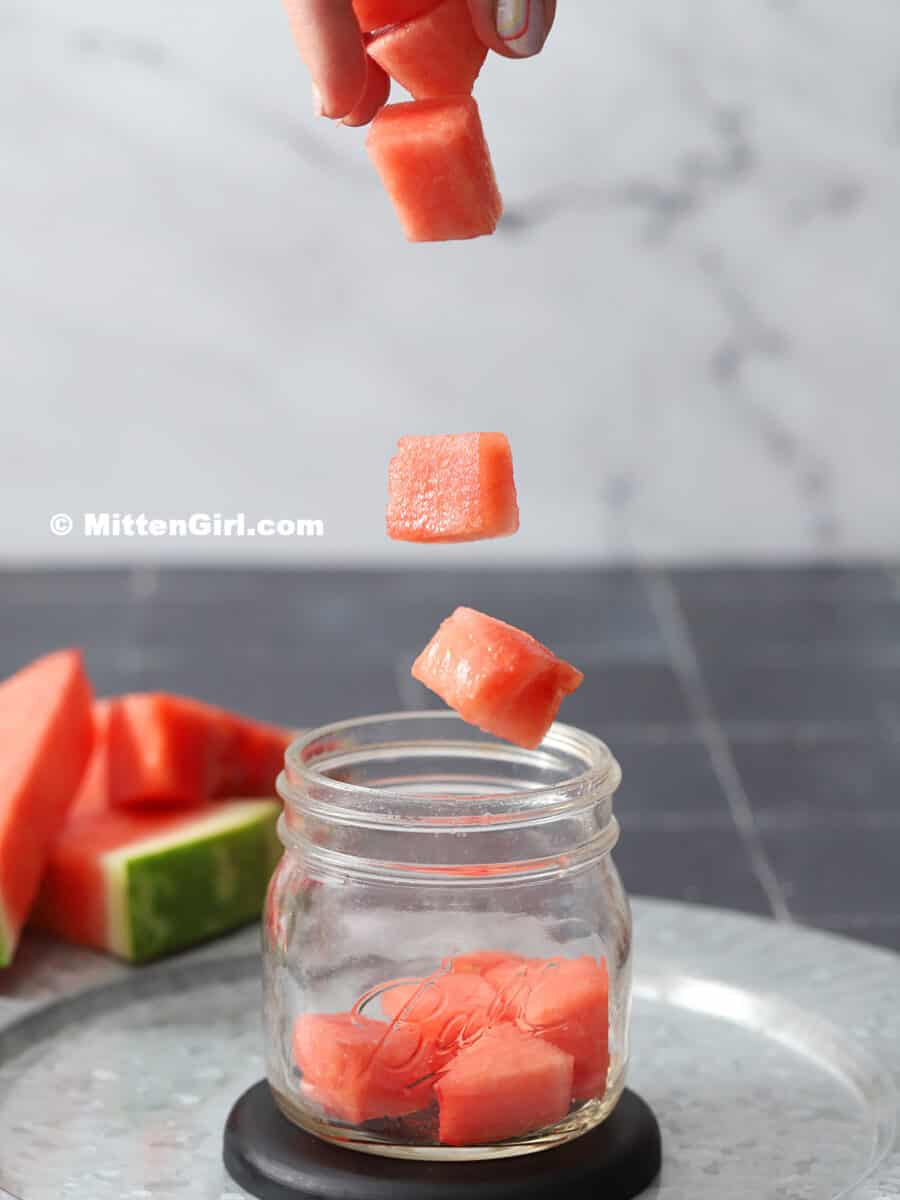 Chunks of watermelon being dropped into a mason jar.