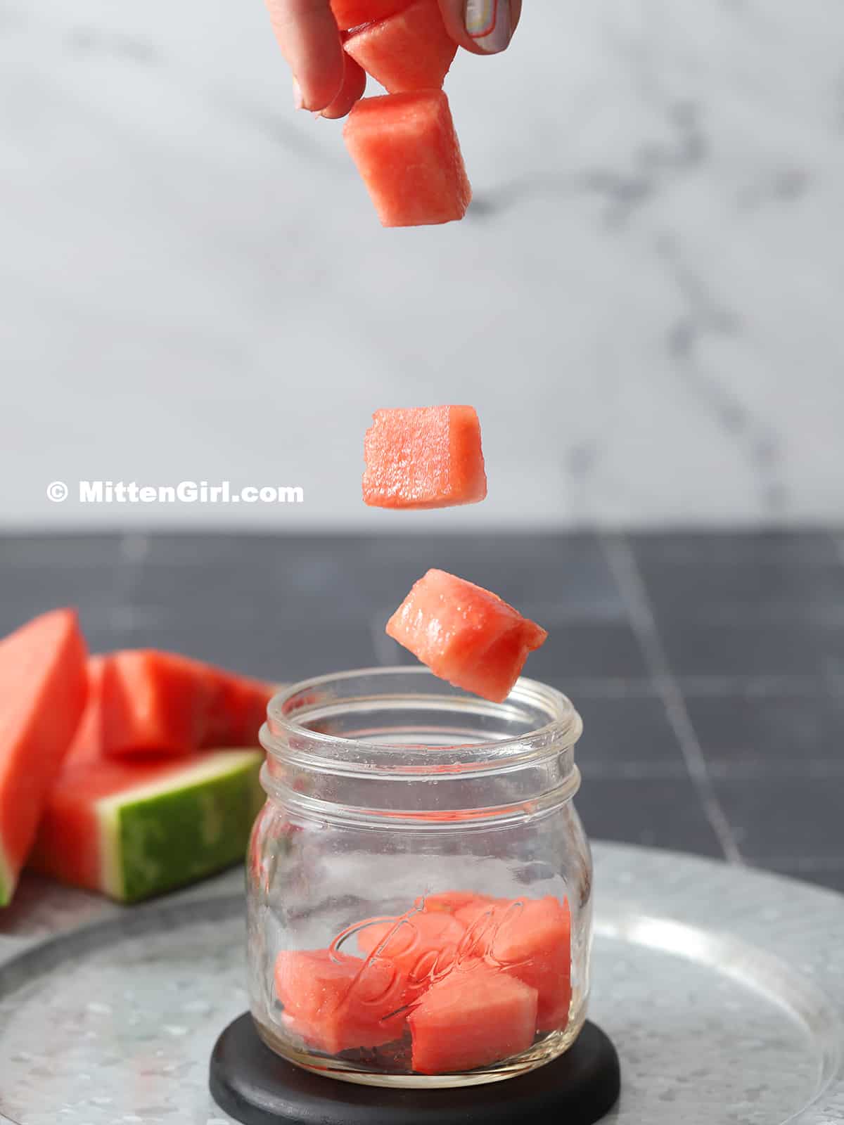 Chunks of watermelon being dropped into a mason jar. 