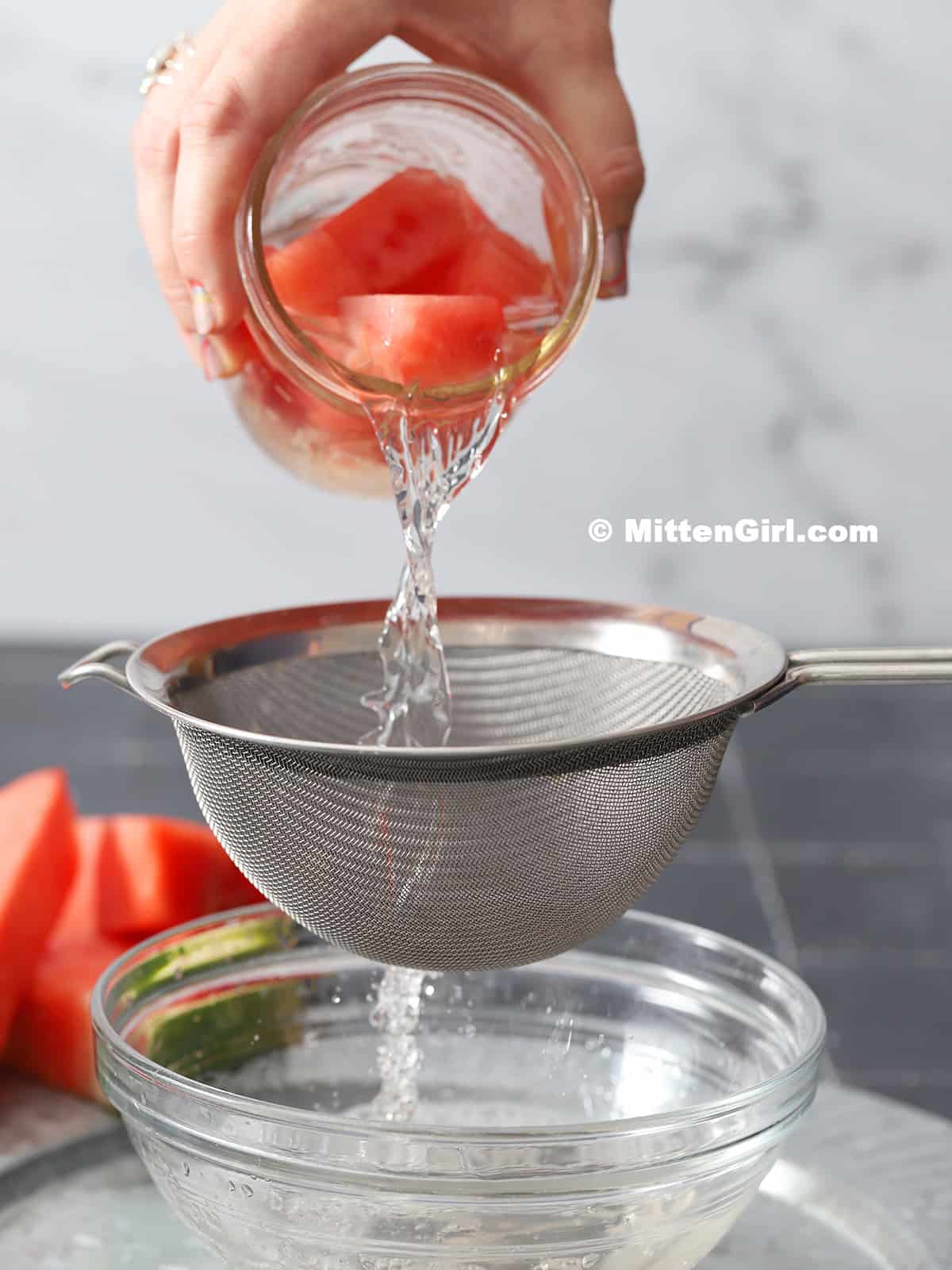 Watermelon infused vodka being poured through a fine mesh strainer held over a bowl. 