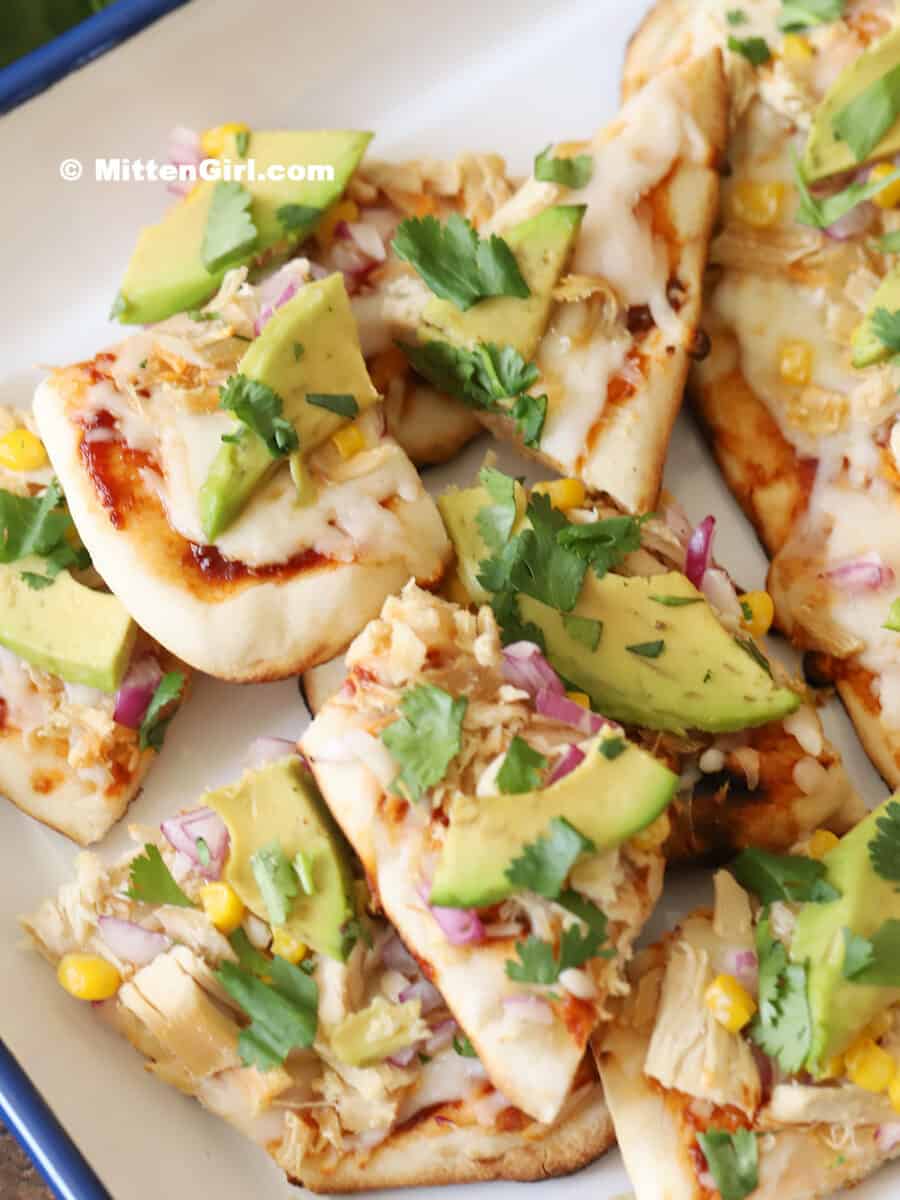 Slices of Grilled BBQ chicken flatbread pizza piled on a platter.