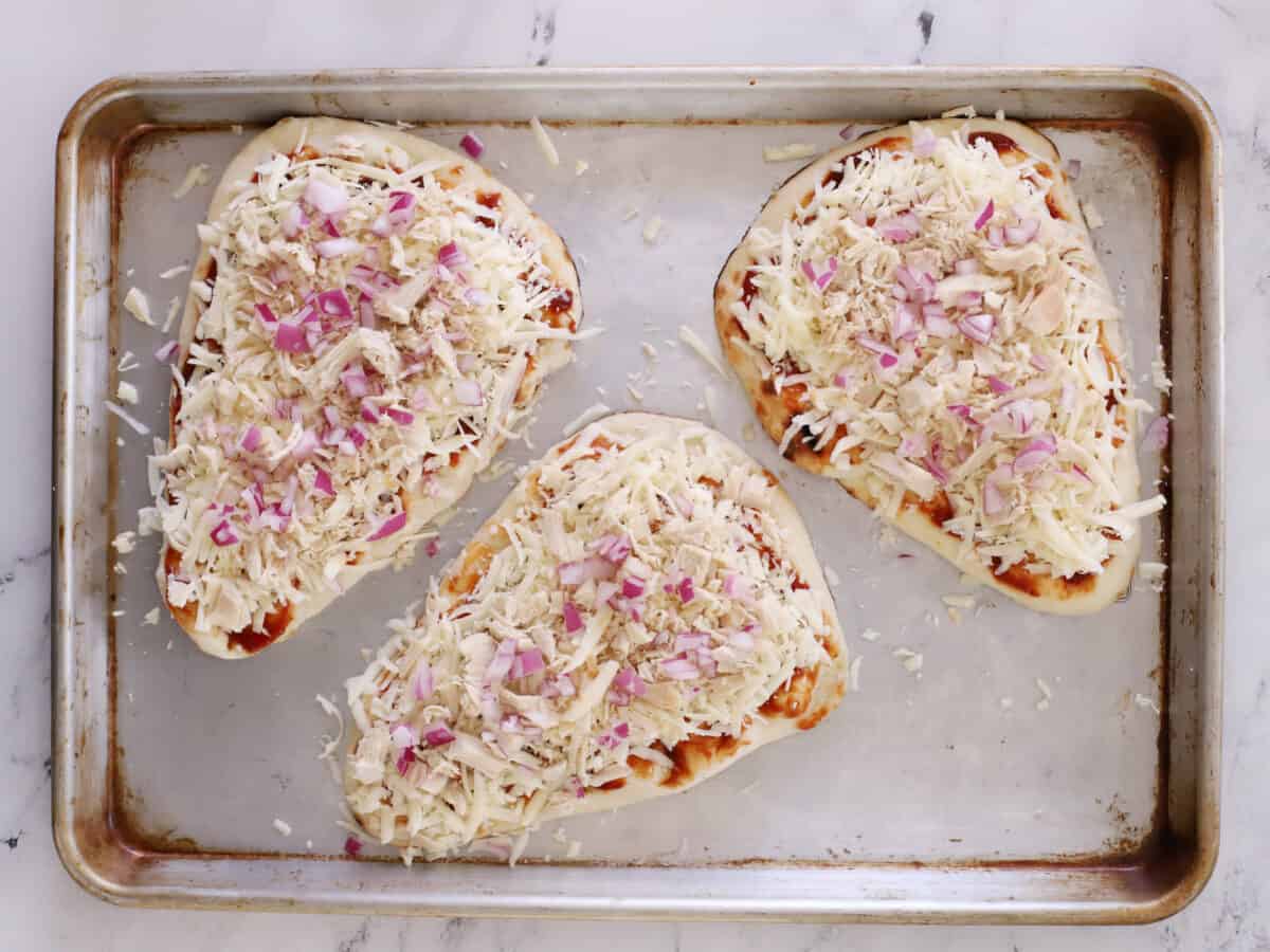 Flatbread on a sheet pan, topped with chicken, cheese, and red onions.