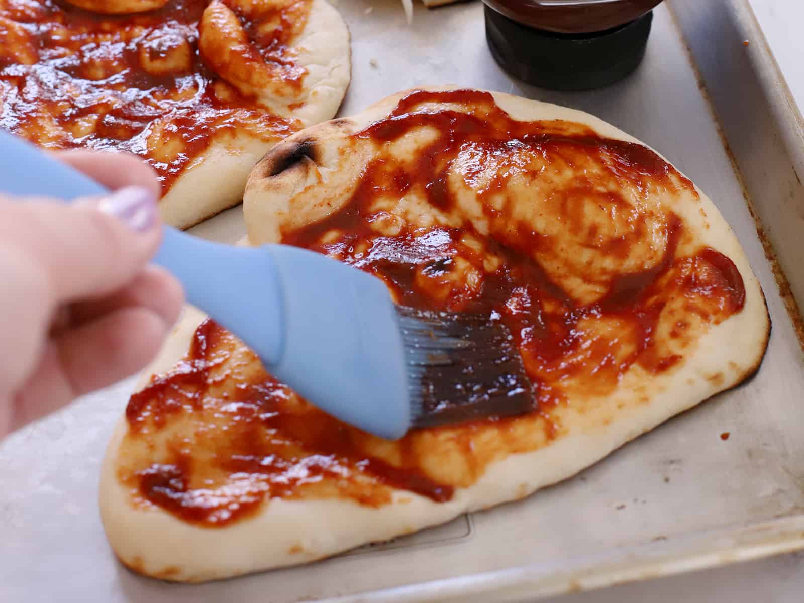 Barbecue sauce being spread on a piece of flatbread.