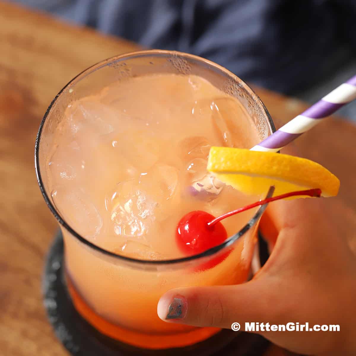 Glass filled with mocktail drink and garnished with a cherry and orange slice.
