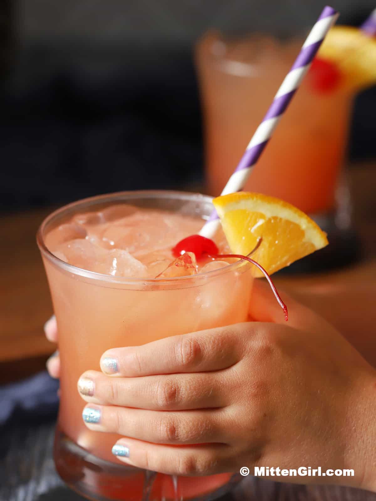 A child's hand picking up a glass full of mocktail. 