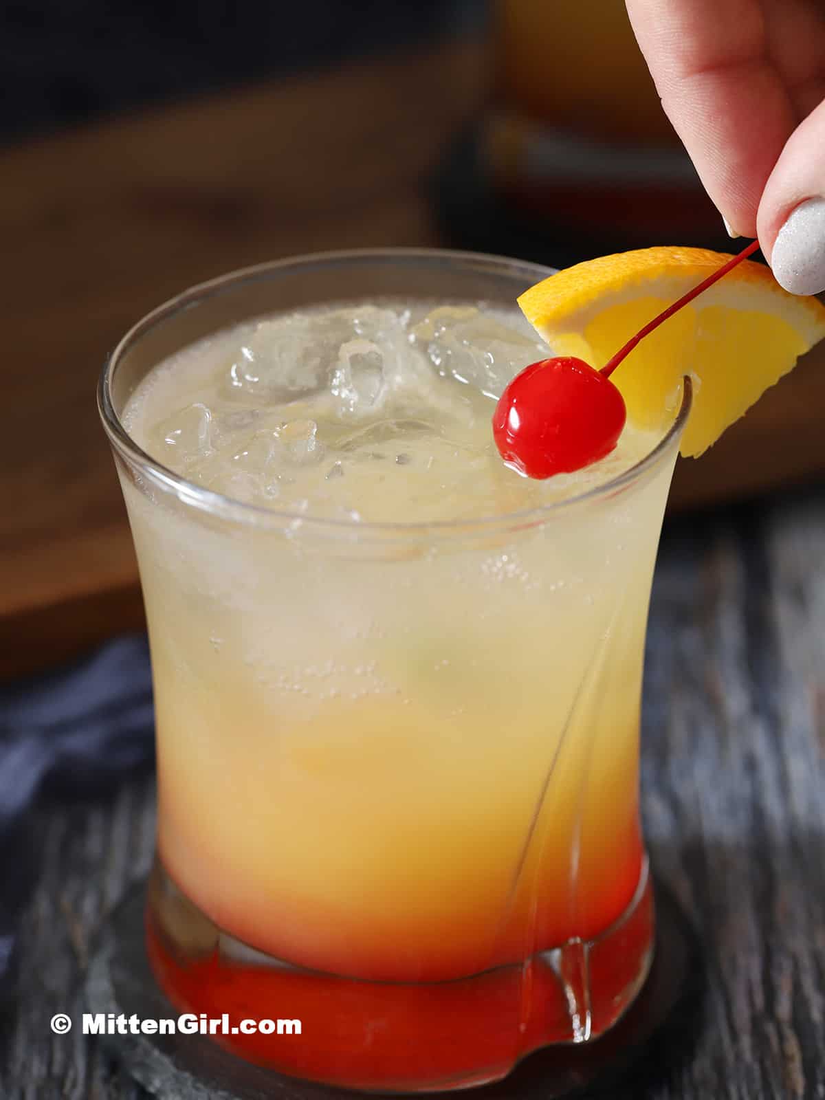 A hand placing garnish on the side of a glass filled with mocktail.  