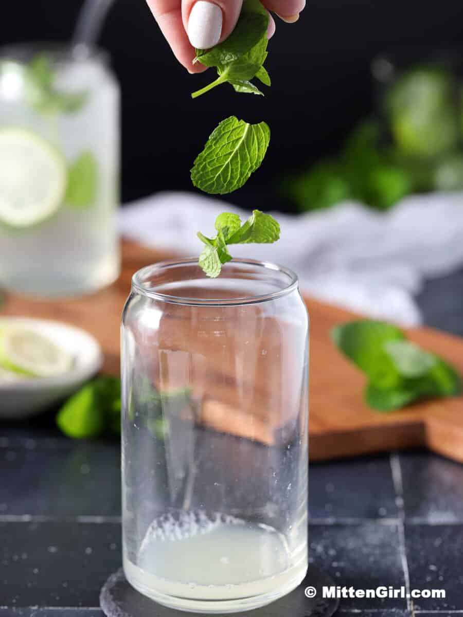 Mint leaves being dropped into a glass with lime juice in it.