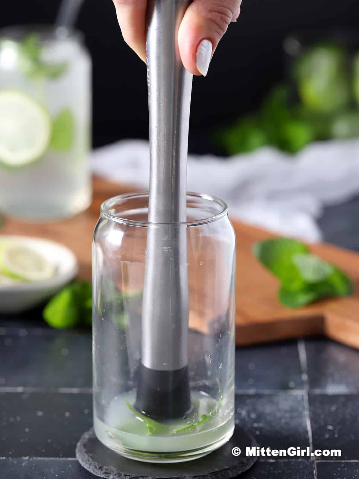 Muddling lime juice and mint leaves in a glass. 