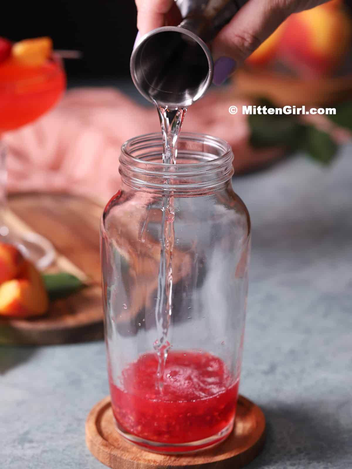 Raspberry vodka being poured into a cocktail shaker.