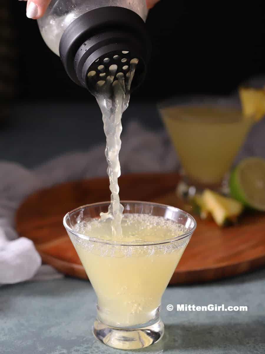 A pineapple vodka martini being poured from a cocktail shaker.