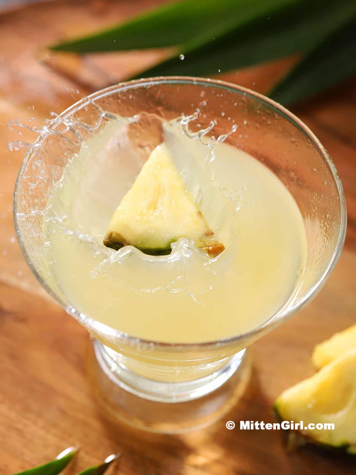 A pineapple wedge splashing down into a martini glass full of cocktail.