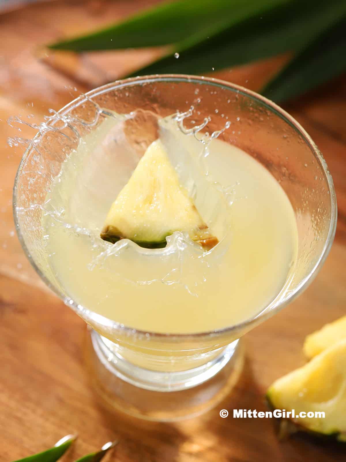 A pineapple wedge splashing down into a martini glass full of cocktail. 