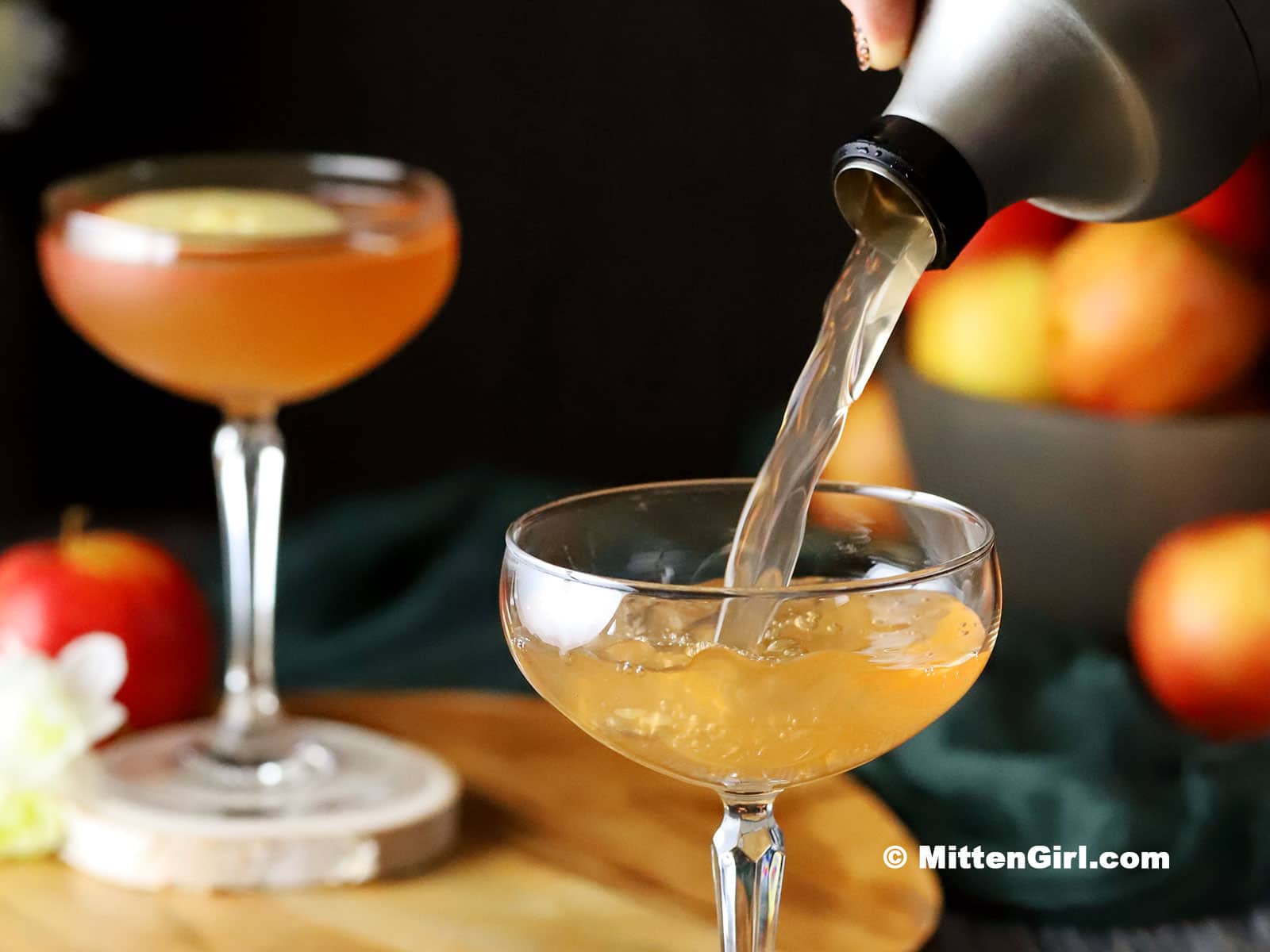 A cocktail shaking pouring an apple orchard cocktail into a coupe glass.