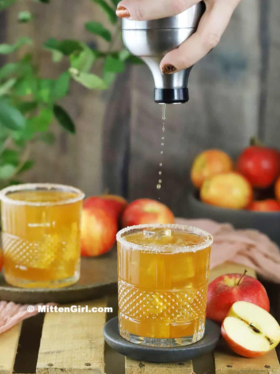 A hand pouring caramel apple cocktail into a rocks glass filled with ice.
