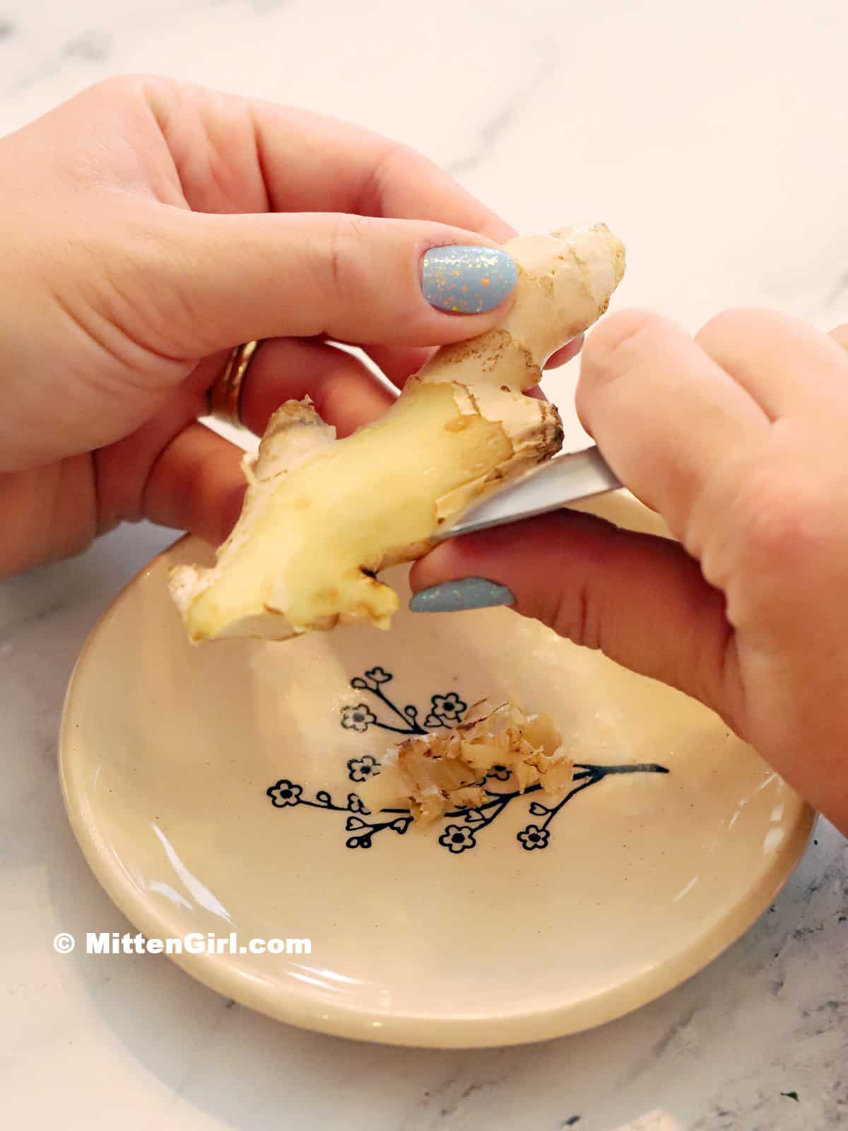 Hands peeling a piece of ginger root using a spoon.