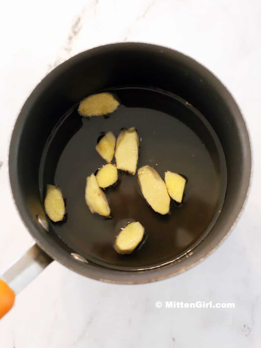 Slices of ginger floating in a pot of syrup.