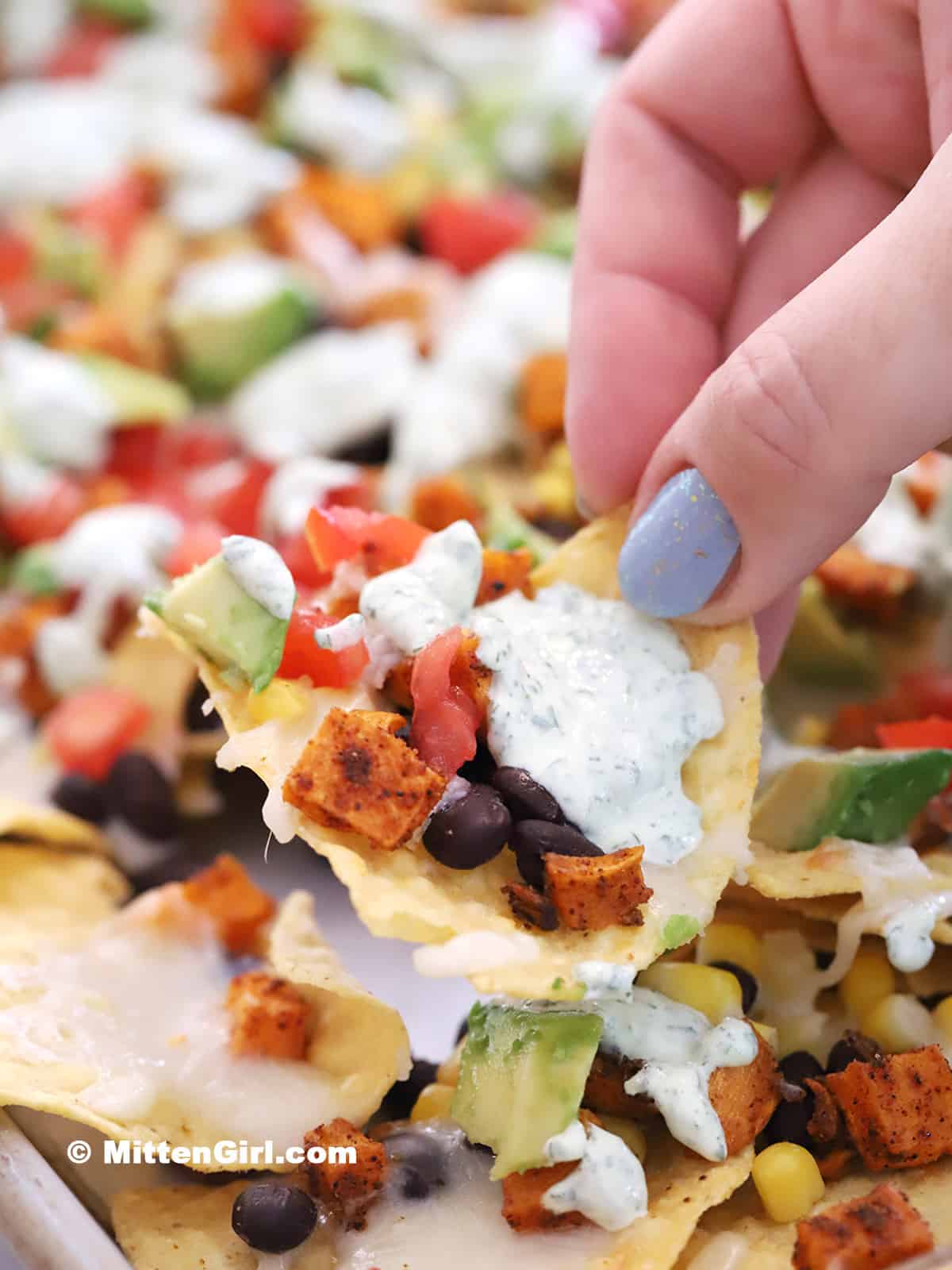 A hand picking up a chip from a tray of vegetarian nachos.