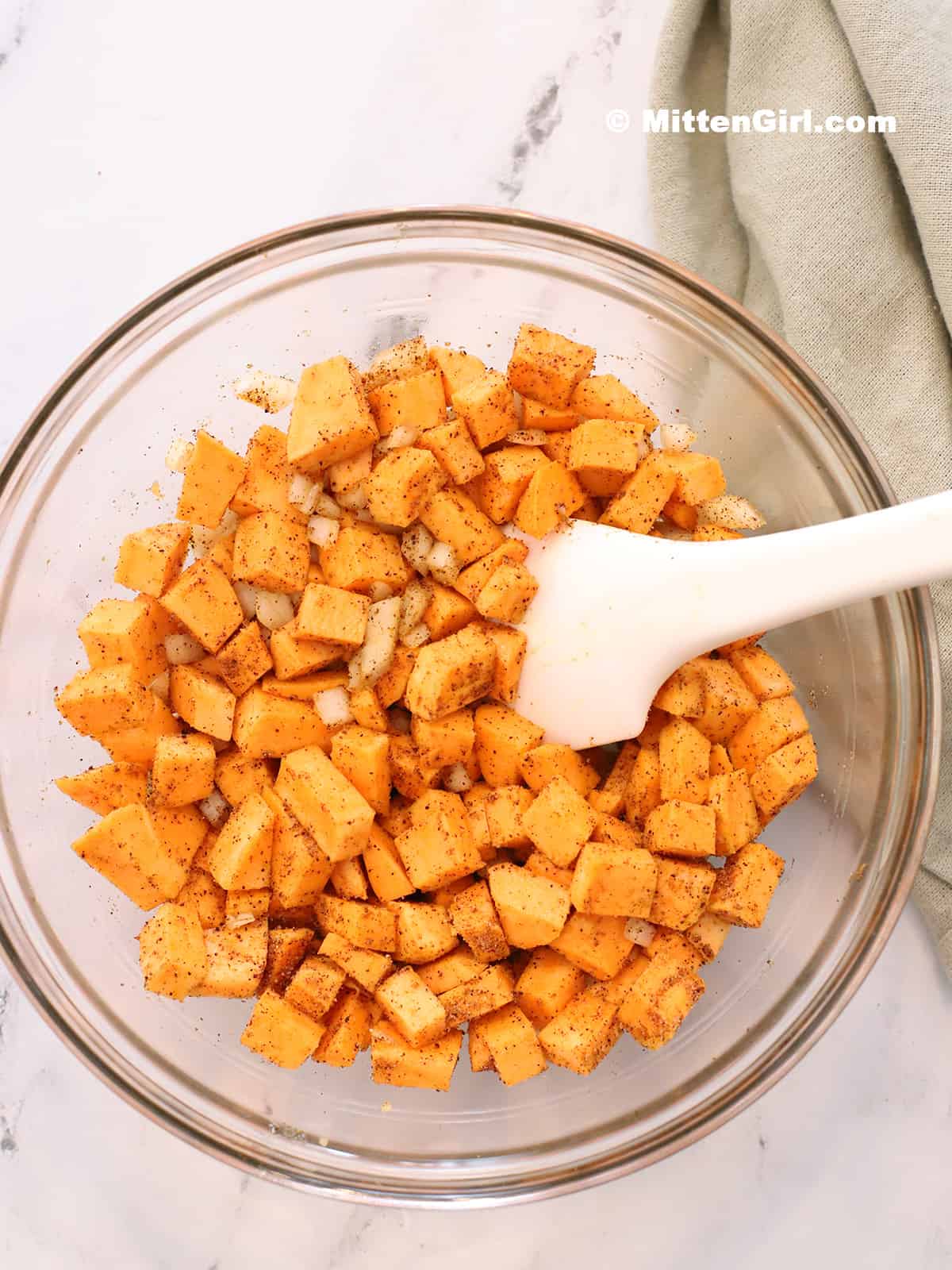 A bowl of diced sweet potatoes, onions, oil, and spices mixed together.