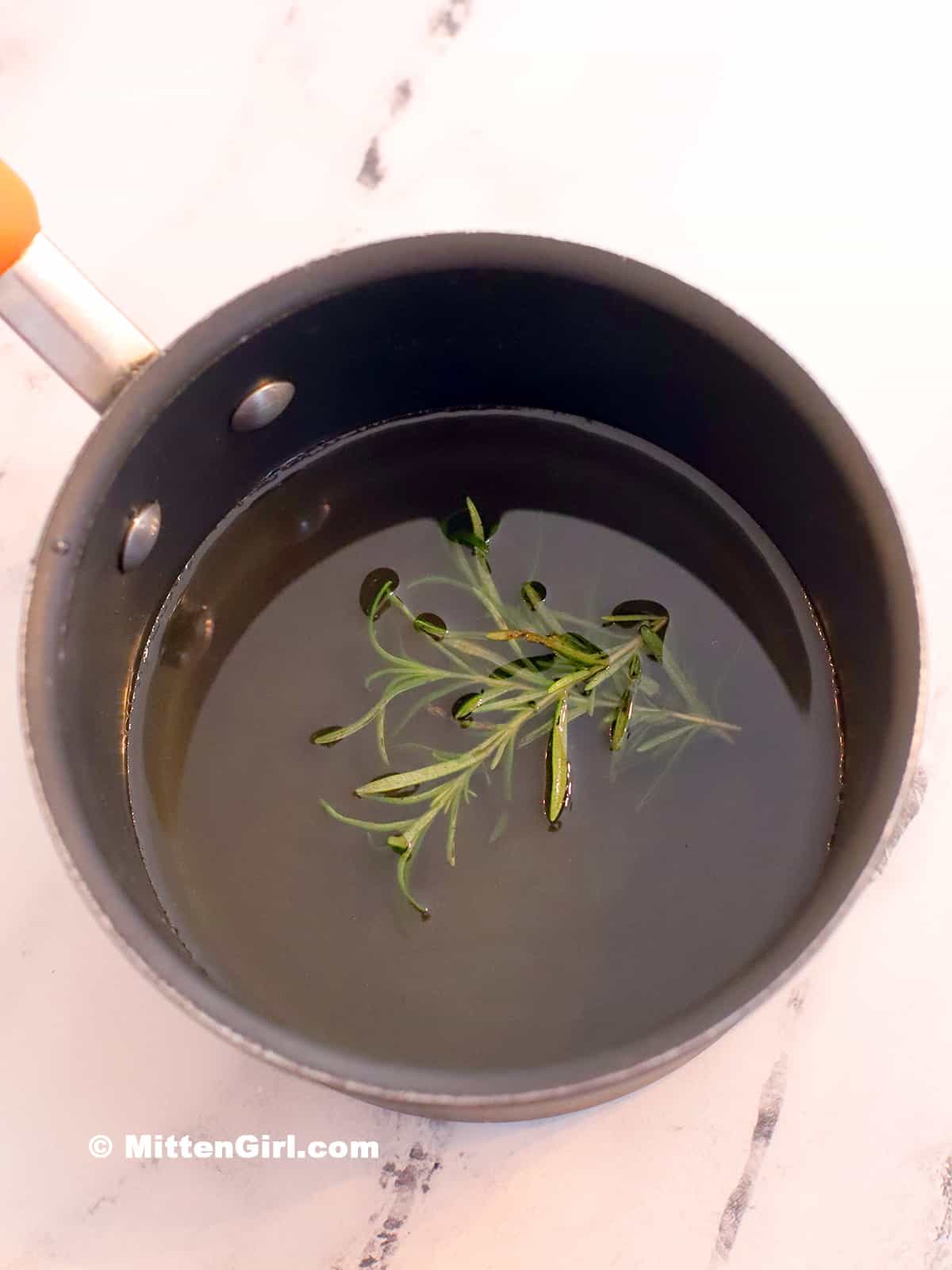 Sprigs of rosemary in a pot of hot syrup. 