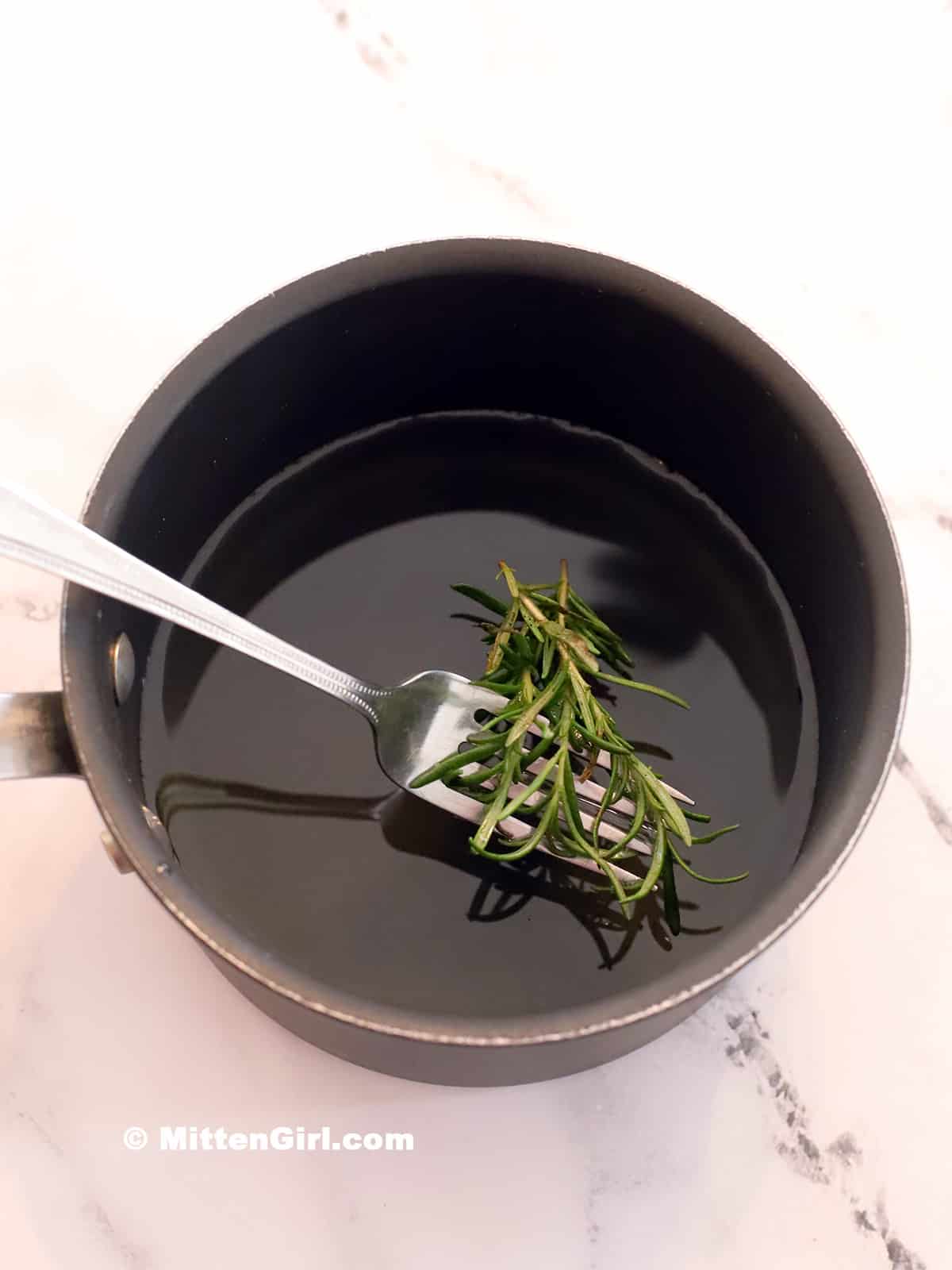 Sprigs of rosemary being lifted out of a pot by a fork.