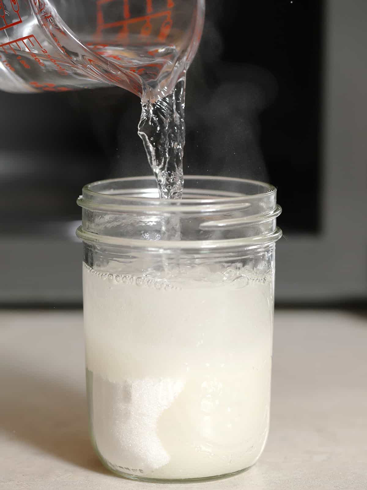 Hot water being poured into a mason jar of white sugar. 