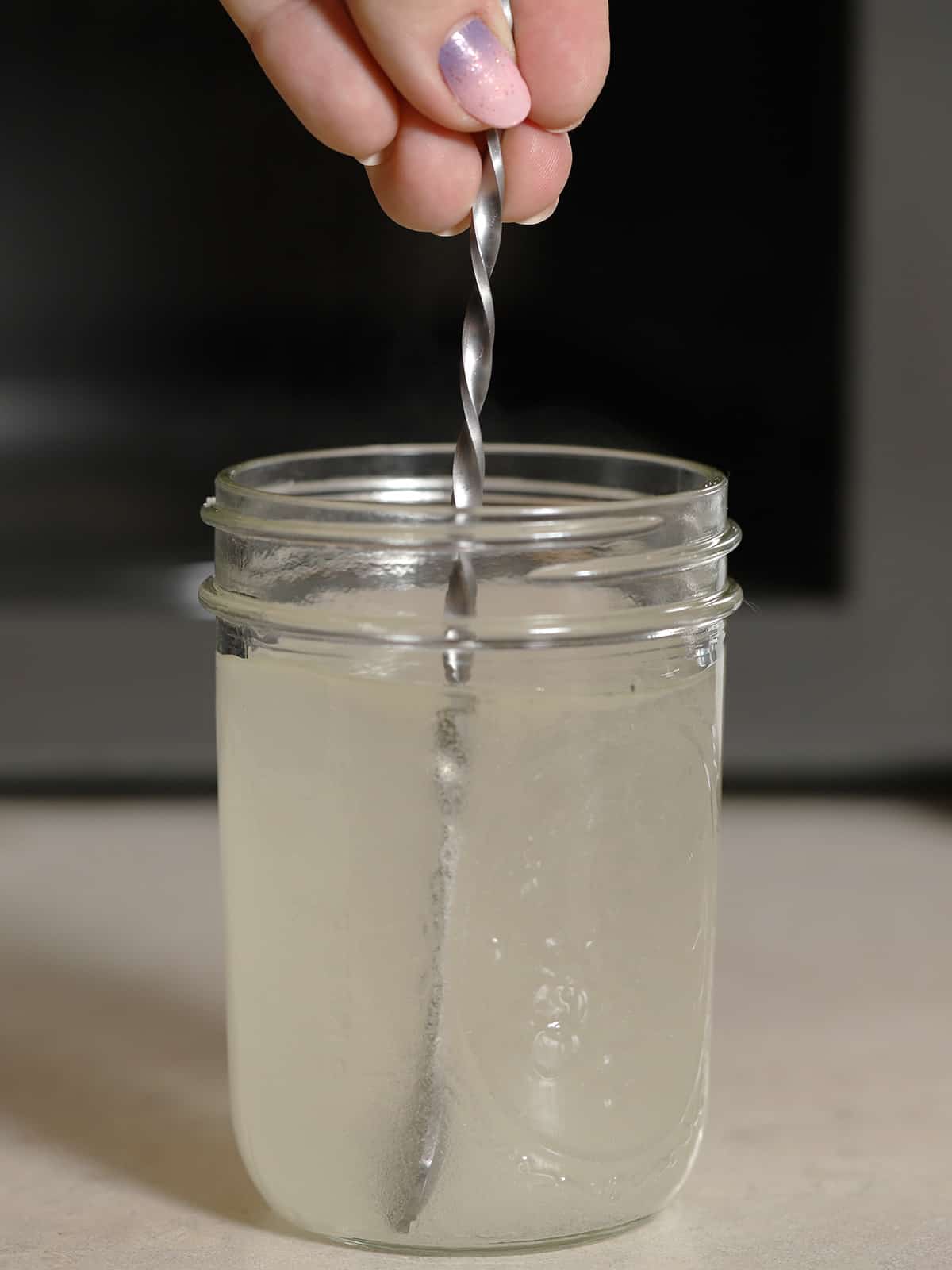 A hand stirring a jar of simple syrup. 