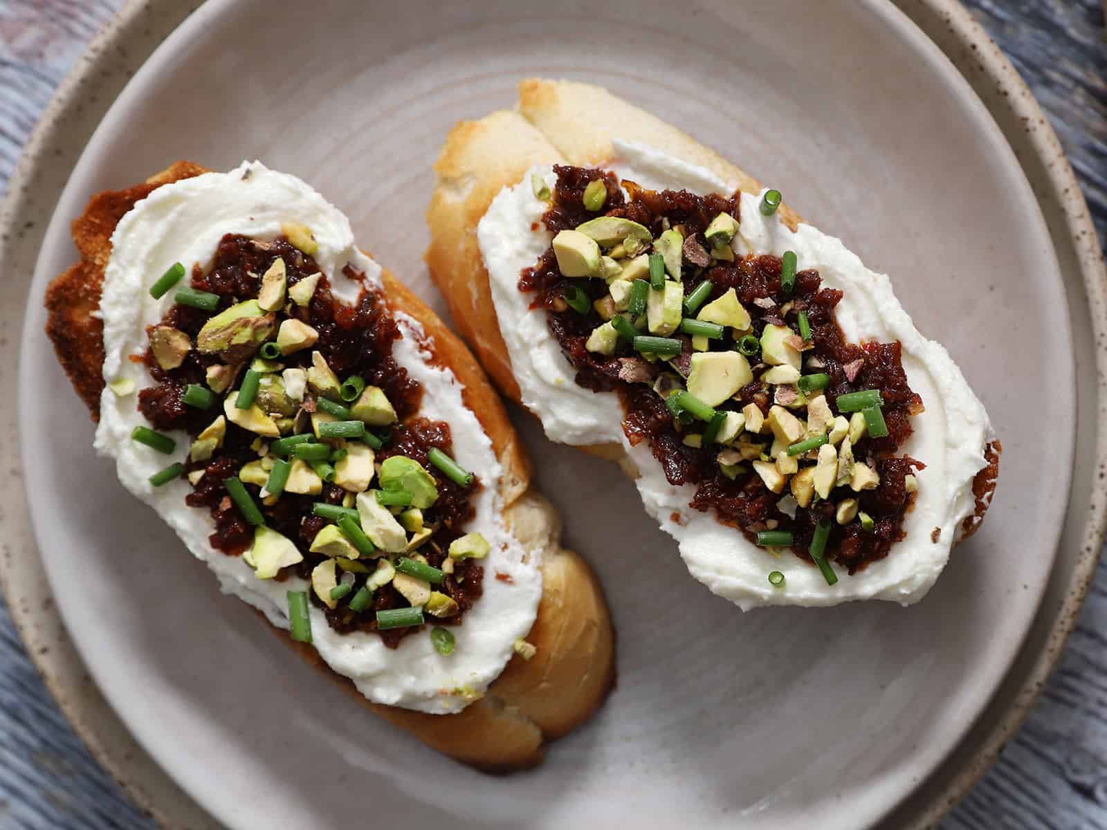 A plate with 2 pieces of whipped feta bruschetta on it.