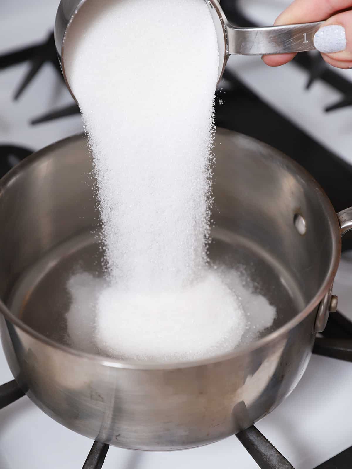 Sugar being poured into a pot of water. 