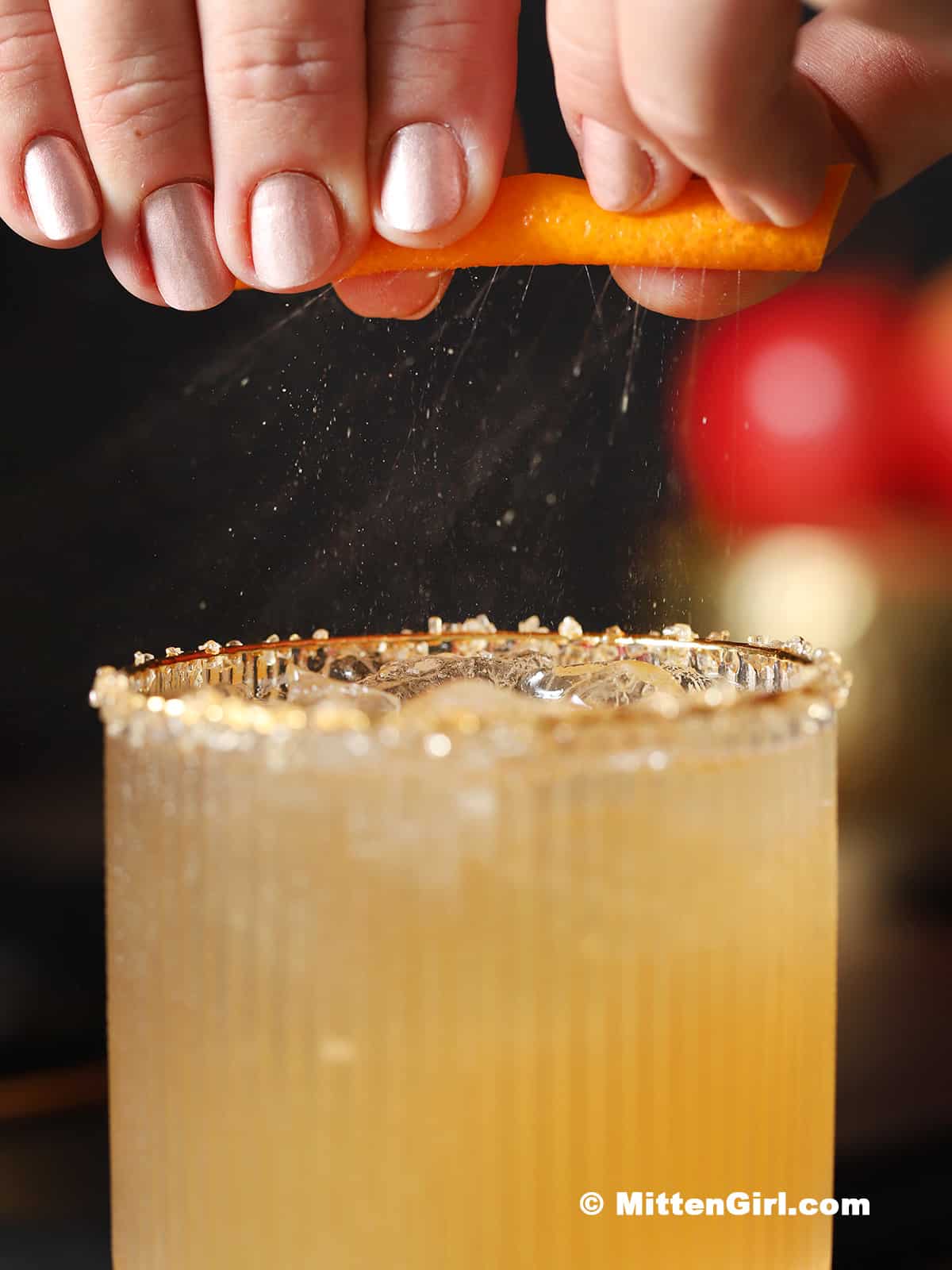 An orange peel being squeezed over a glass of apple mocktail.