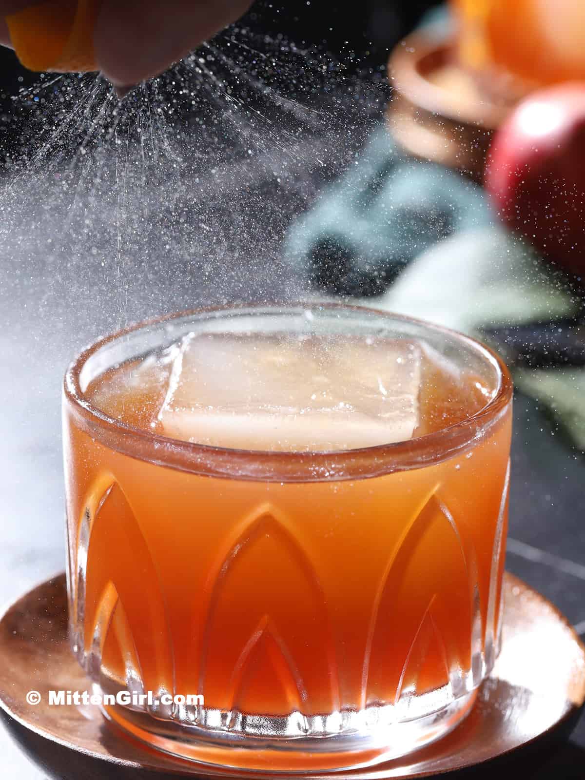 An orange peel being expressed over a cocktail.