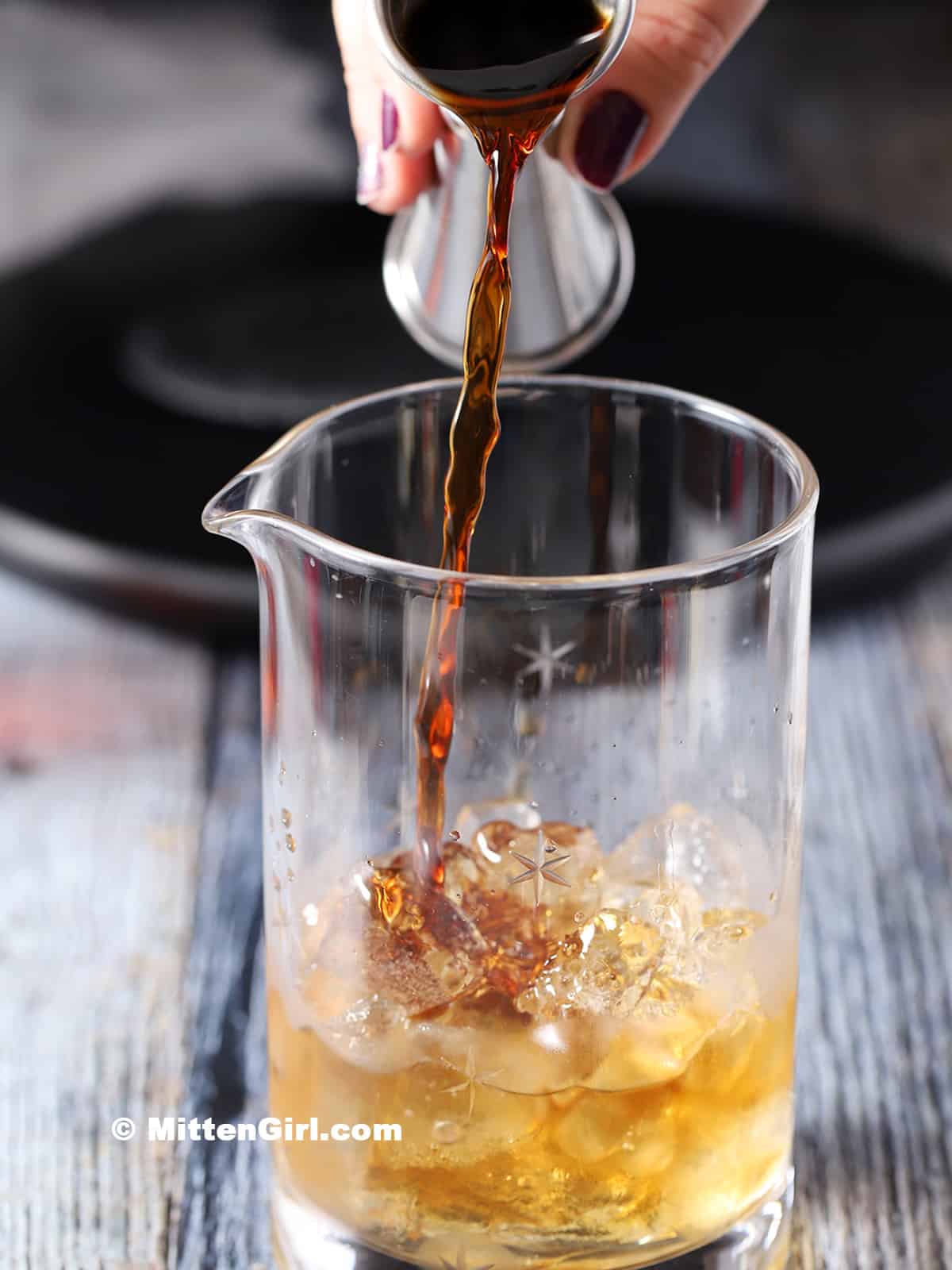 Coffee being poured into a mixing glass filled with bourbon and ice.