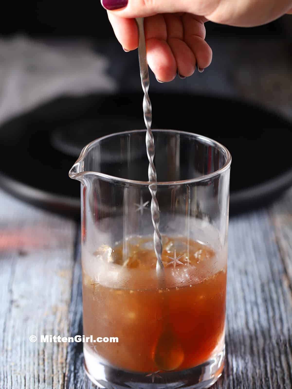 A hand stirring a cocktail in a mixing glass with a bar spoon.