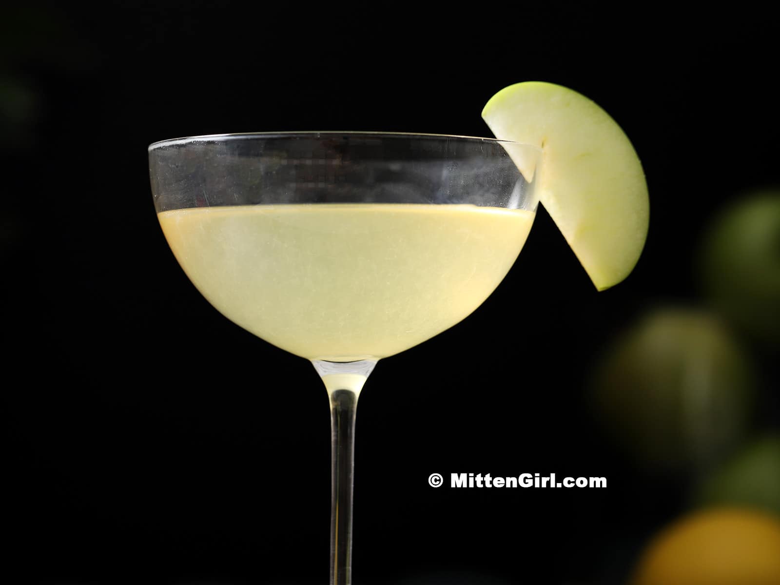 Green Apple Martini in a coupe glass garnished with a slice of apple.